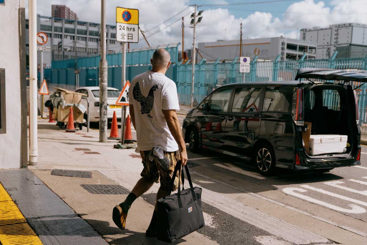 A photo of Matt Abergal, a chef from Hong Kong walking towards a black transport van carrying a black Herschel Supply Company Insulated Alexander Zip Tote
