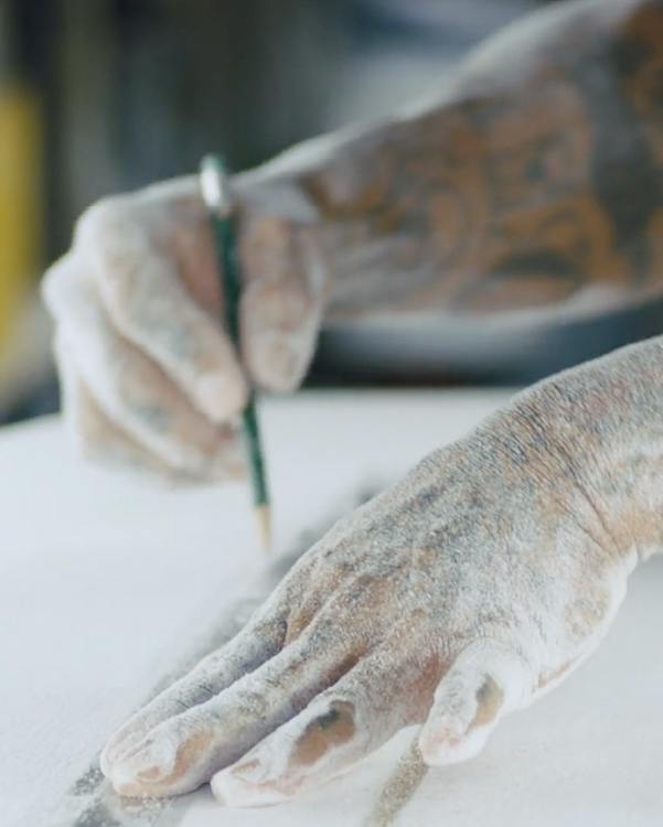 Dust covered hands draw a line on a surfboard