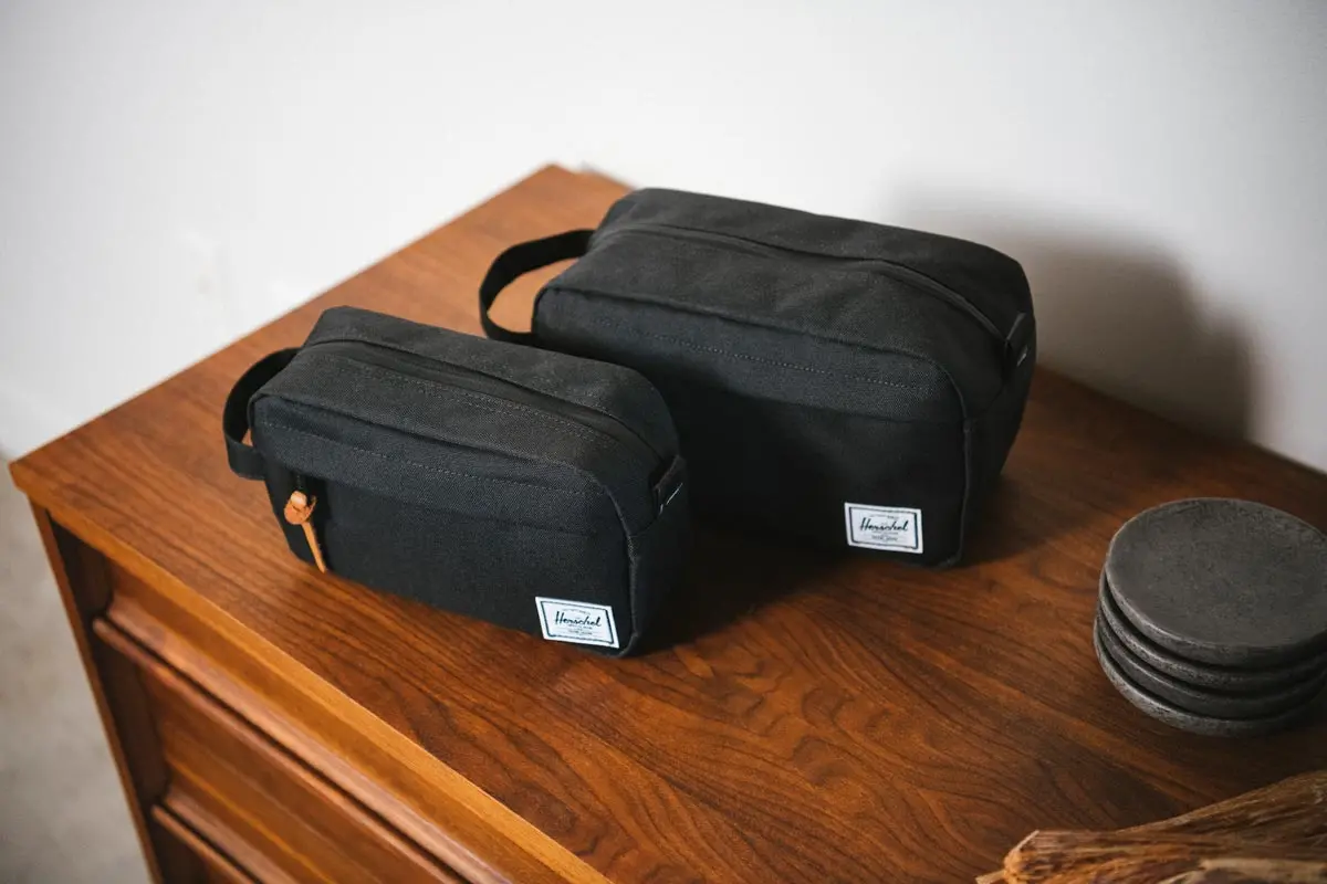 A black Herschel Chapter Carry On Travel Kit & Herschel Chapter Travel Kit sitting on a wood dresser.